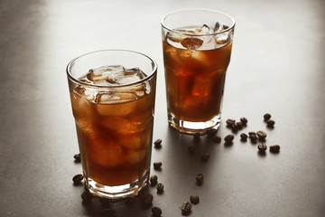 Glasses of iced coffee and roasted beans on grey background