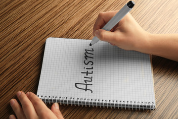Human hands writing word AUTISM in notebook