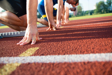 Close-up side view of cropped people ready to race on track field