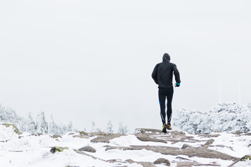 runner in black warm sportswear running in wind and fog on the high mountain trail in the winter - Powered by Adobe