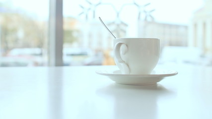 White cup on the table in coffee against a background window.