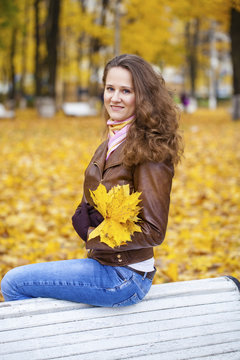 Young woman sitting on bench in the autumn park