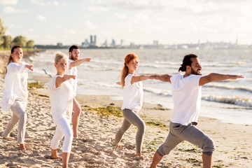 people making yoga in warrior pose on beach
