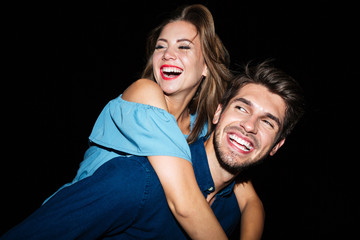 Smiling man holding girlfriend on his back at night