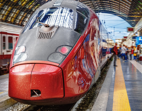 Fototapeta High-speed train at the railway station in Milano, Italy. Express train from Milano to Florence parking at plathorm. Passenger staing nearby.