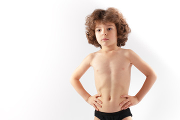 Little curly boy with no shirt shows her body. Gray background.