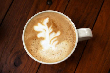 A cup of latte with drawing sprigs on milk foam on wooden table