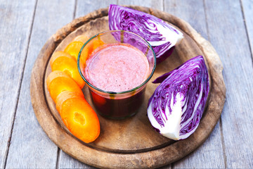 A glass of healthy mixed carrot and purple cabbage juice on a wooden table.