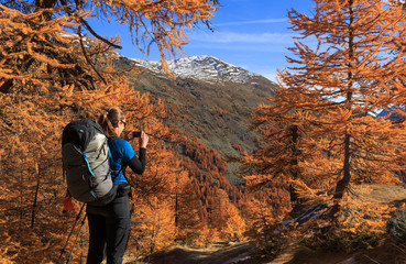 Female hiker photographing the warm autumn colors in the Claree valley, France.