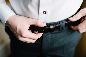 Man corrects belt. Groom, white shirt, formal suit