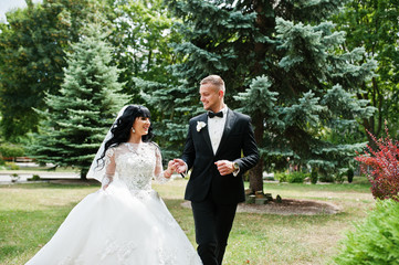 Cheerful wedding couple running holding hands on green garden co