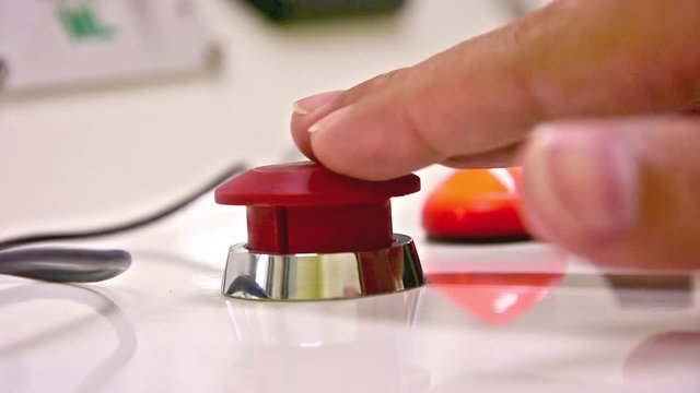Hand presses the red emergency button on the panel