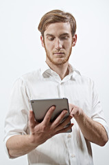 Young Adult Male in White Shirt Holding, Looking at and Touching the Screen of a Digital Tablet
