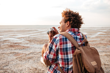 Back view of happy man taking pictures on the beach