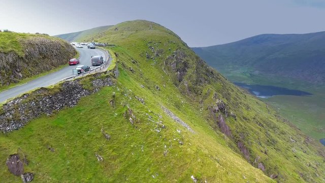 The green hills on the cliff of the SKyroad with lots of tourists on their cars parked on the top in Ireland
