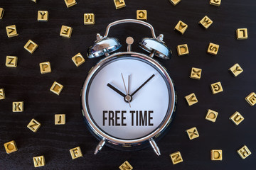 Free time - Alarm clock on wooden table with letters