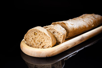 Fresh sliced baguette on wooden oblong plate on black background