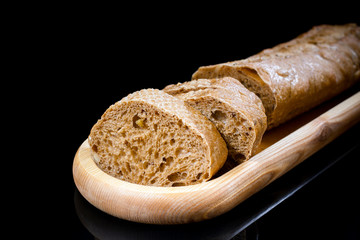 Close-up fresh sliced baguette on wooden oblong plate on black b
