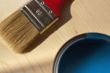 Red paintbrush painting wooden furniture in blue color, close up