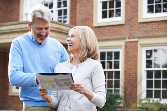 Mature Couple Standing Outside House Looking At Property Details