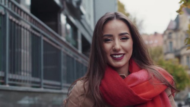Close up view of extraordinary natural beauty, in a red scarf, and with a cup of coffee. Gorgeous woman smiling towards the camera while walking down the city street.