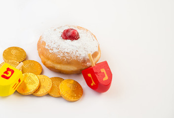 Fresh donut, chocolate coins and wood dreidels for Hanukkah celebration. Selective focus.
