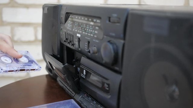 The hand turns the other side and inserts the cassette into the old tape recorder, push play. Close-up.