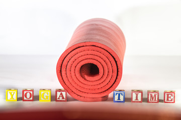 Rolled up yoga mat with words yoga time spelled with wooden alphabet letter blocks 