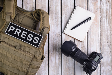 Body armor for journalist, notebook and camera/Body armor for journalist with patch "press", notebook with pen and camera on wooden table.Top view