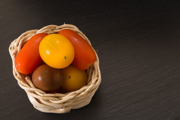 Colorful cherry tomatoes in wicker basket, on black background.