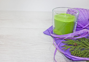 Green apple aromatic candle with lilac ribbon, lilac napkins and branch cypress on white wood...