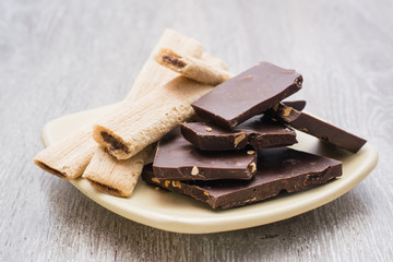 Кусочки темного шоколада с миндалем и печенье с начинкой из шоколада на блюдце на деревянном столе 