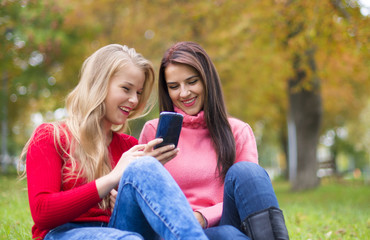Fototapeta premium Two girls in park with a mobile phone