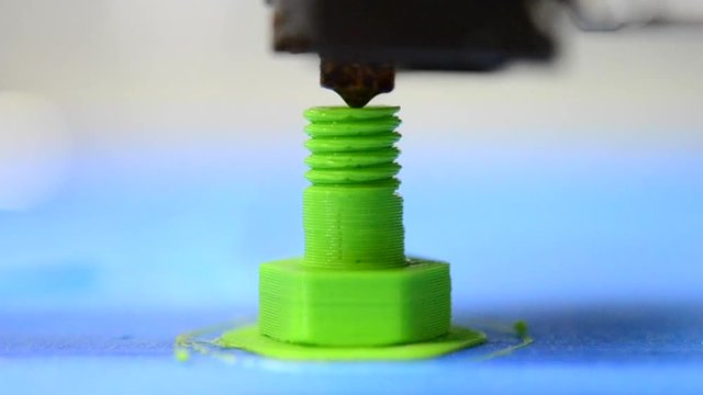 HD 1080 3D printer prints from the plastic figure in the form of a bolt closeup. 3D printer makes or printing bolt model, screw green colour close-up on blue flat surface