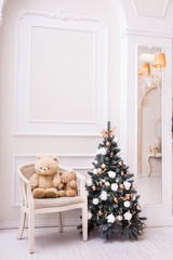 Small Christmas tree near chair with teddy bear. Vertical