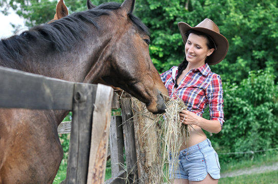 young woman in  cowgirl style feeding horse
