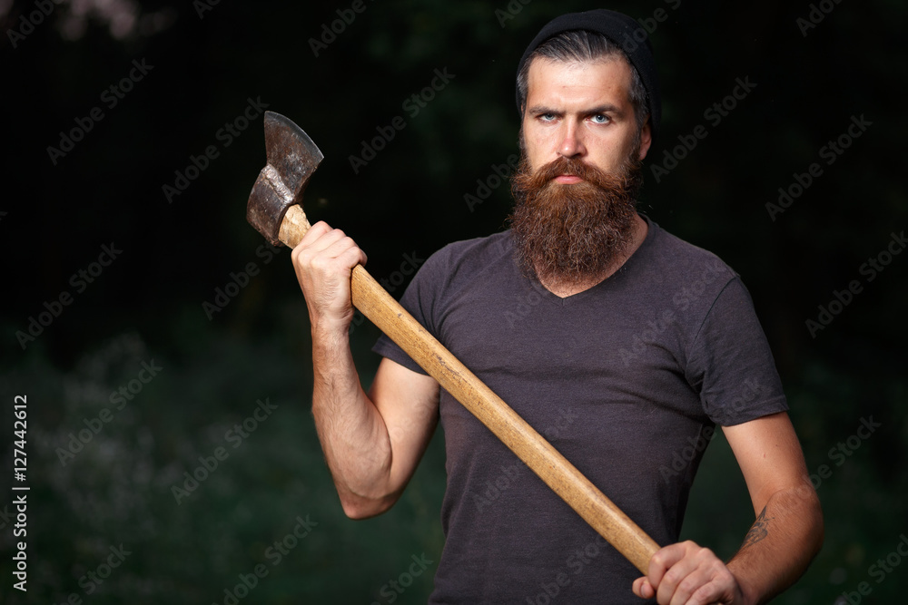 Wall mural brutal brunette bearded man in warm hat with a hatchet in the woods on a background of trees