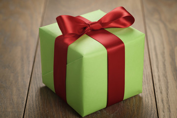 Obraz premium simple green paper gift box with red ribbon bow on oak table