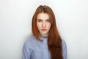 Young serious angry redhead beautiful woman in shirt portrait on a white background