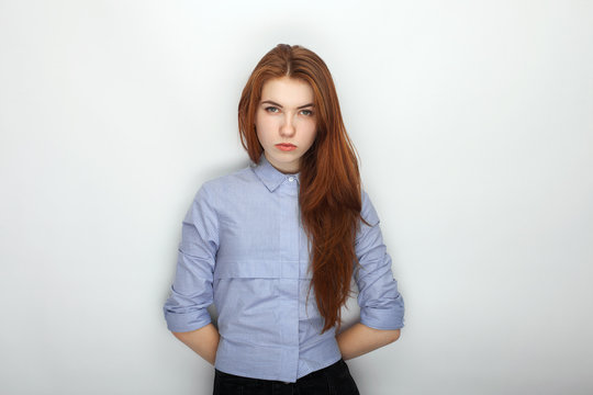 Young serious angry redhead beautiful woman in shirt portrait on a white background hidden hands