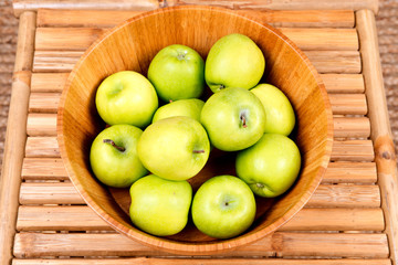 Organic granny smith apples in wooden bowl on bamboo table