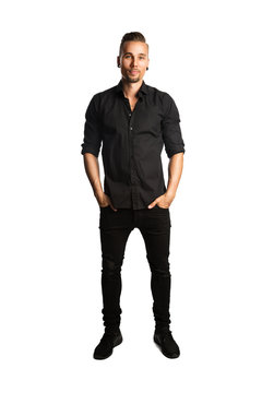 A handsome man wearing black jeans and a black shirt standing against a white background smiling.