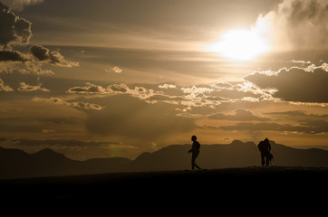 Fototapeta premium Silhouettes of two people walking on White Sand Dunes during sunset in New Mexico