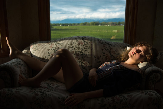 Young woman sleeping on sofa in rural country house with sunlight on face