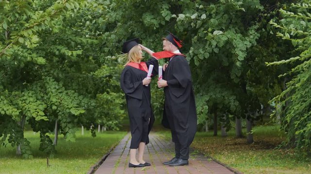 Windy weather, pair of graduates standing in park with diplomas, wind of change