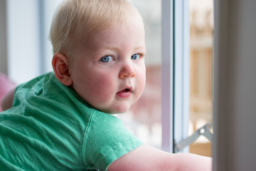 Baby boy opening a window with child proof locks keeping him saf