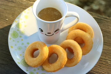 A cup of coffee and donuts on wooden table in the morning