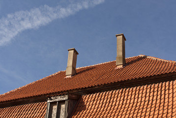 Old tiled roof with chimneys and window against blue sky