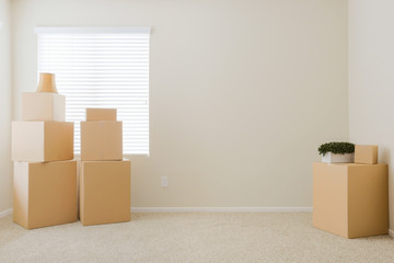 Fototapeta premium Variety of Packed Moving Boxes and Potted Plants In Empty Room with Room For Text.