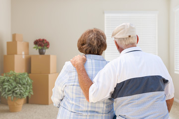 Senior Couple Facing Empty Room with Packed Moving Boxes and Potted Plants.